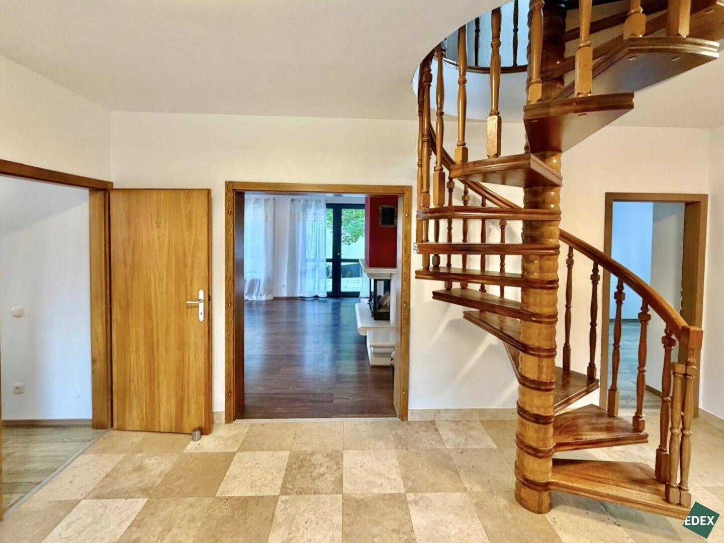 Flur mit Holzwendeltreppe und Zugang zum Wohnzimmer, das durch eine Holztür sichtbar ist.