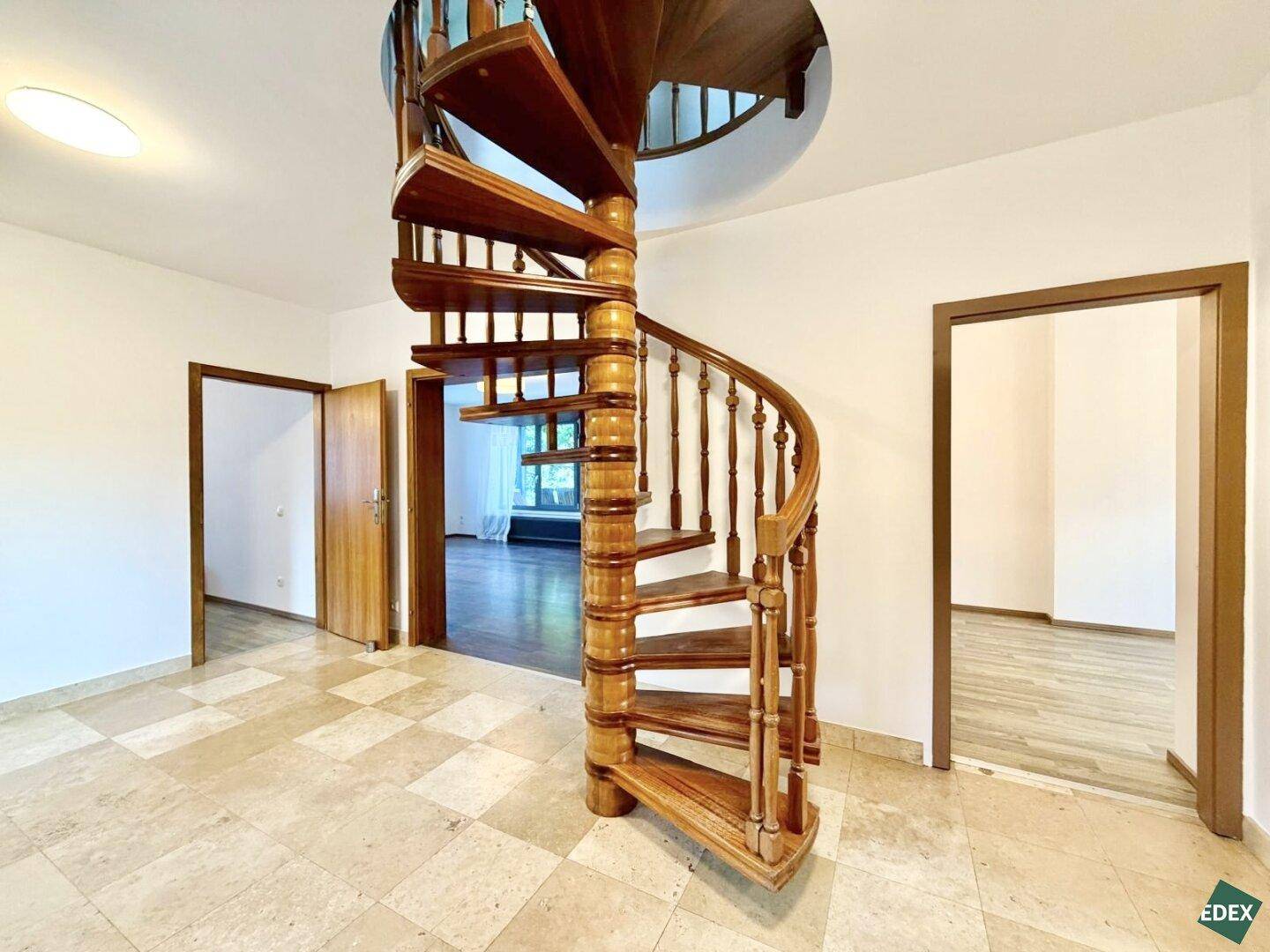 Eingangsbereich mit eleganter Holzwendeltreppe und gefliestem Boden, der zu weiteren Räumen führt.