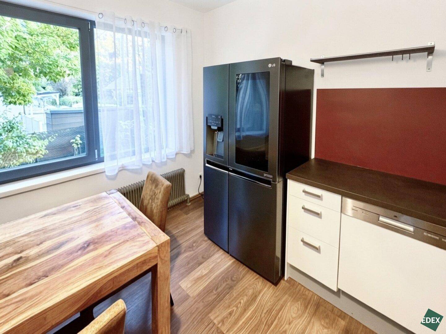 Essbereich in der Küche mit großem Holztisch, schwarzem Kühlschrank und Fenster.