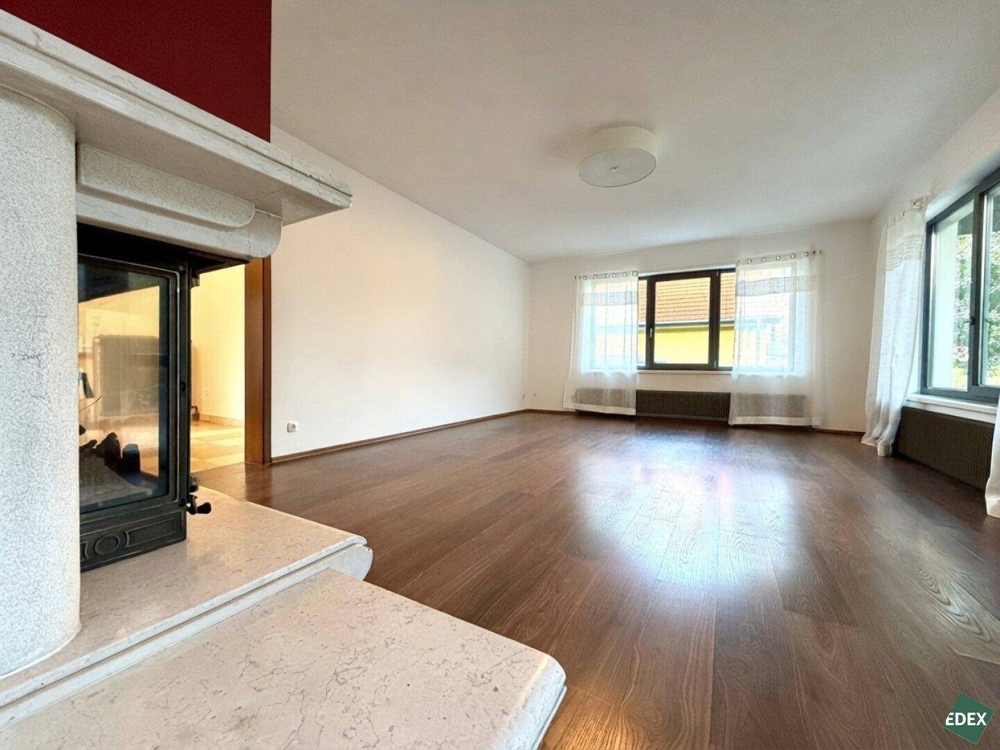 Gemütliches Wohnzimmer mit Kamin, Holzboden und Blick auf die Umgebung durch die Fenster.