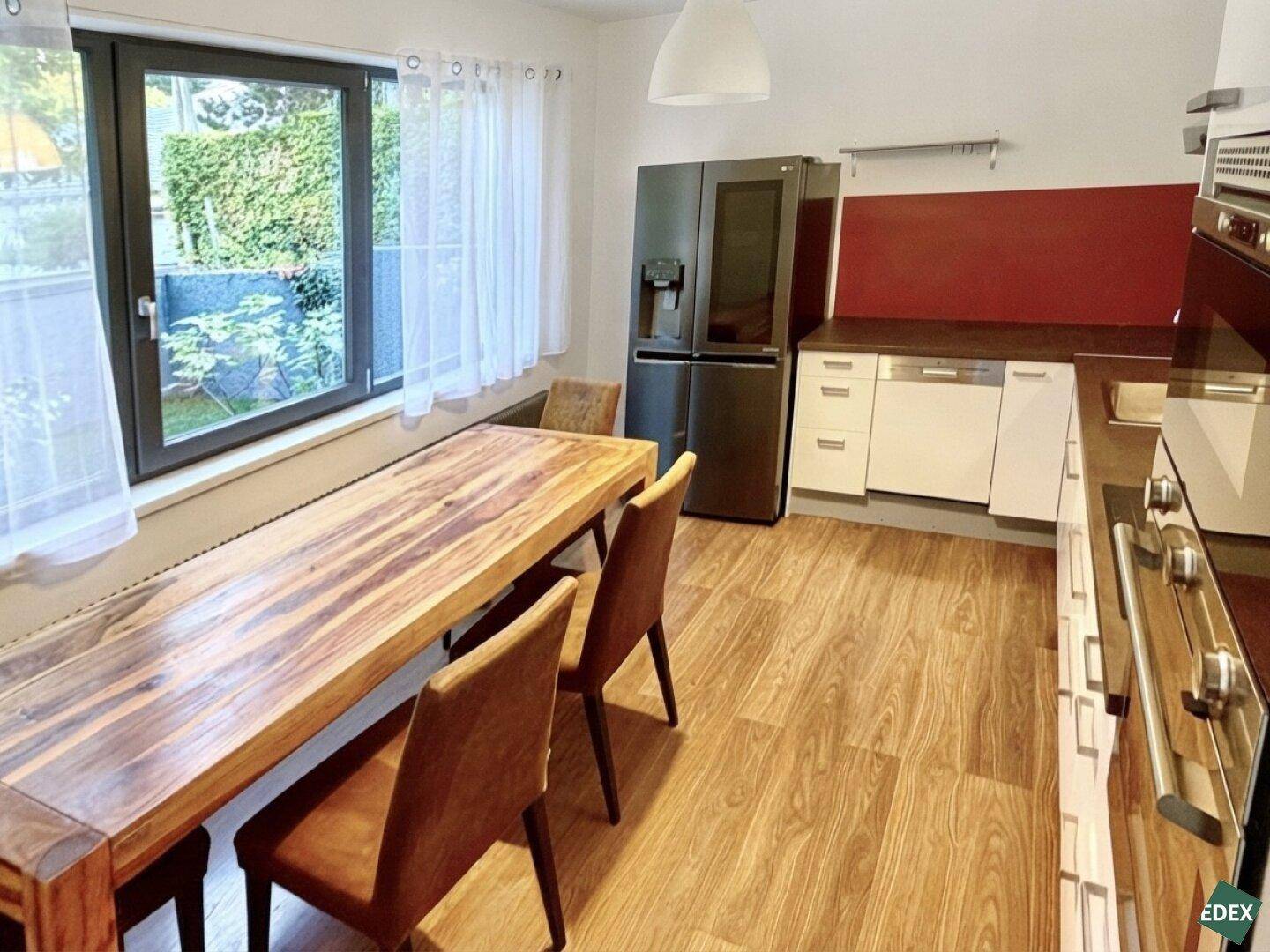 Moderne Wohnküche mit Holztisch, schwarzem Kühlschrank und Fenster mit Blick ins Grüne.