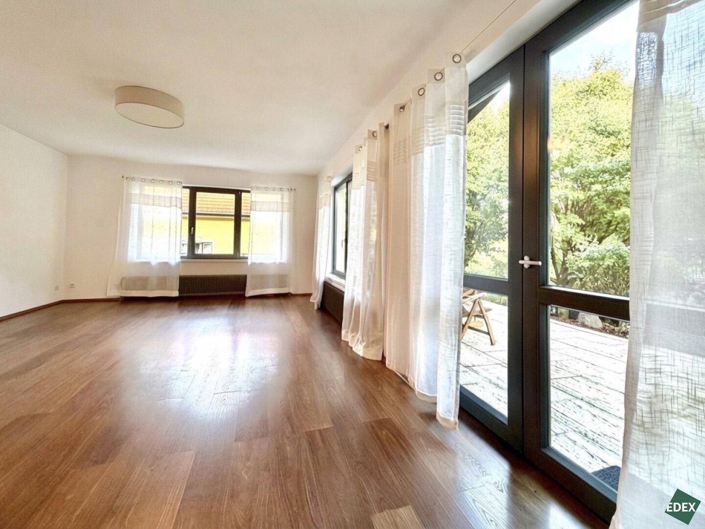 Helles Wohnzimmer mit Holzboden und Zugang zu einem Außenbereich durch große Fenstertüren.