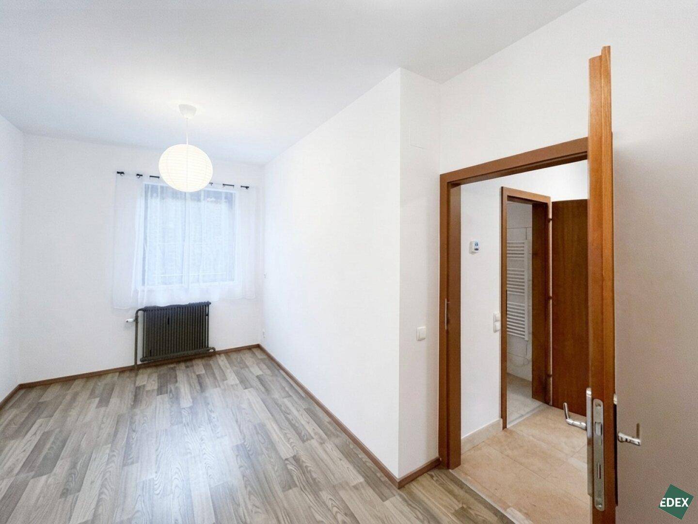 Helles Schlafzimmer mit Laminatboden, weiß gestrichenen Wänden und Fenster.