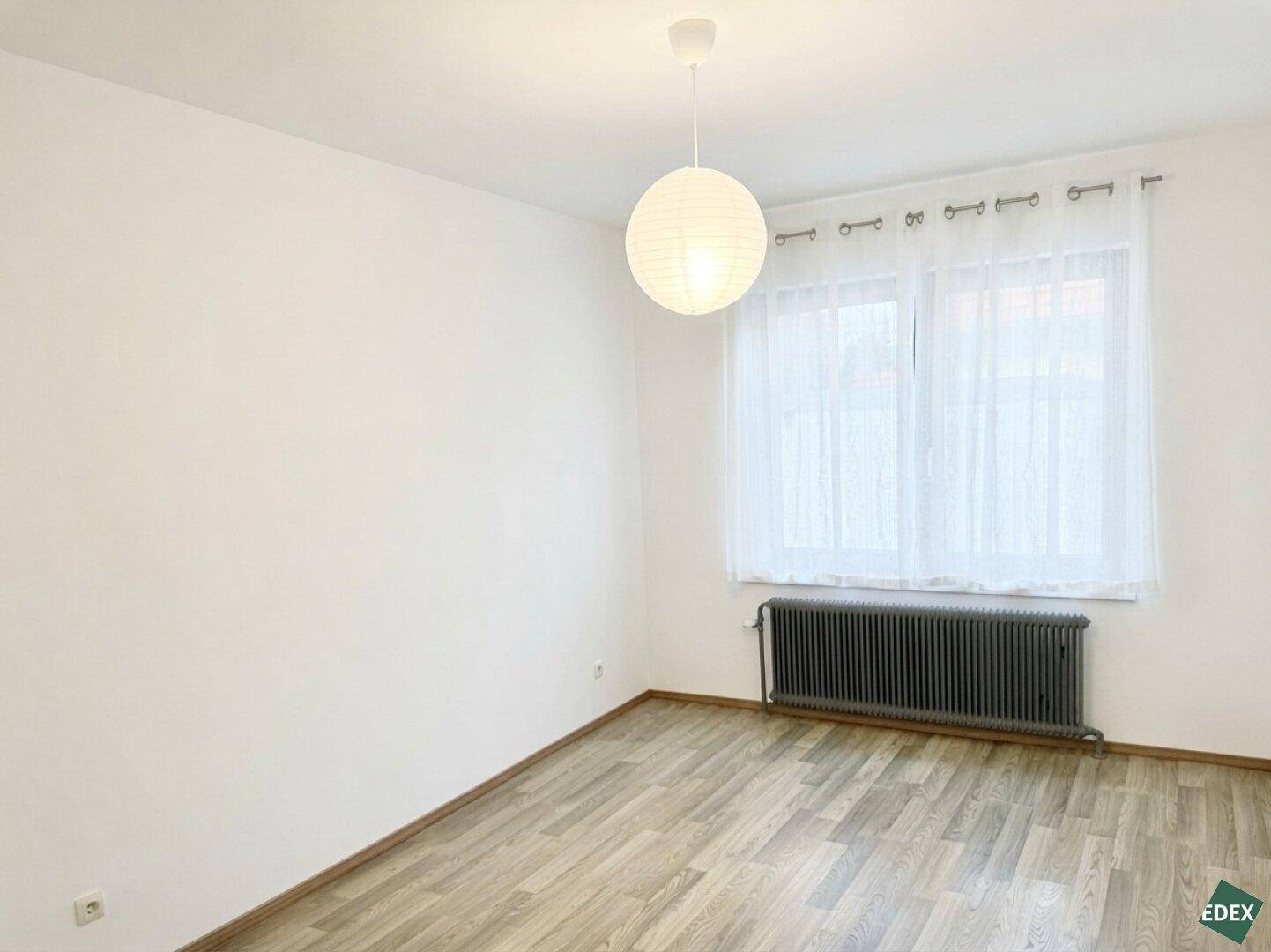 Schlafzimmer mit großem Fenster, Heizkörper und schlichtem, funktionalem Design.