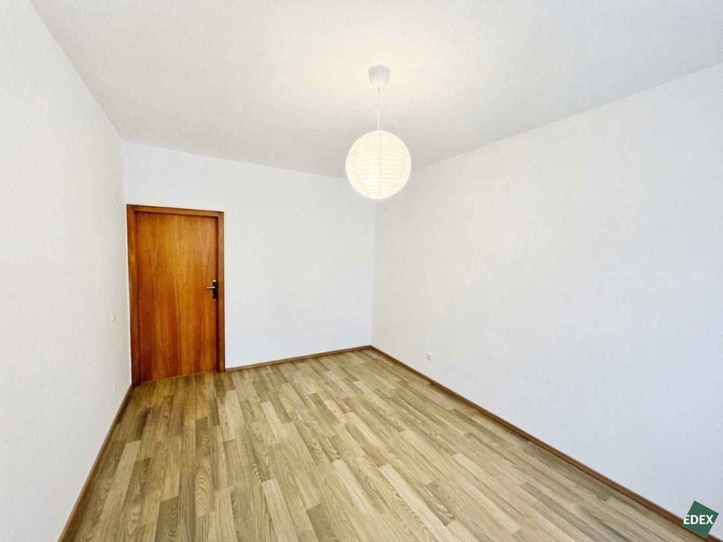 Geräumiges Schlafzimmer mit Laminatboden und Holztür, bereit zur individuellen Gestaltung.