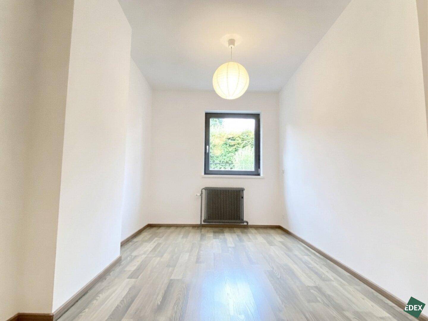Helles Schlafzimmer mit Laminatboden und Fenster, das einen Blick nach draußen bietet.