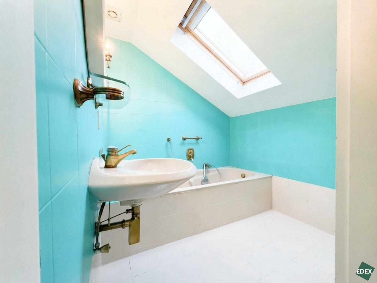 Badezimmer im Dachgeschoss mit blauen Fliesen, Badewanne und Dachfenster.