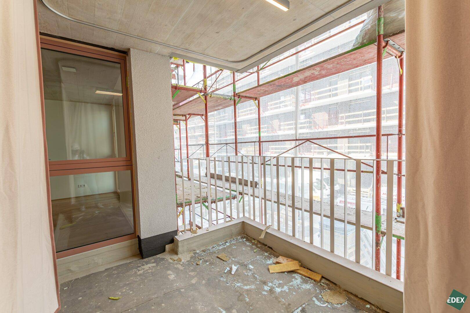 Balkon im Bauzustand mit Betonboden und Blick auf umliegende Gebäude und Gerüste.