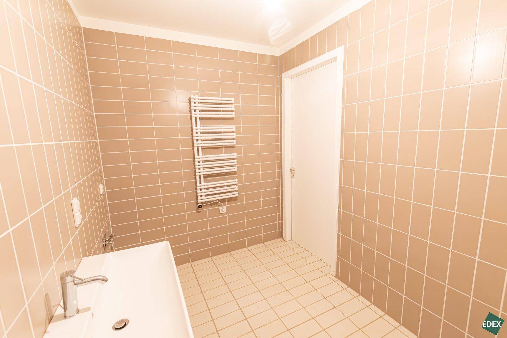 Funktionales Badezimmer mit beigefarbenen Fliesen, Waschbecken und beheiztem Handtuchhalter.