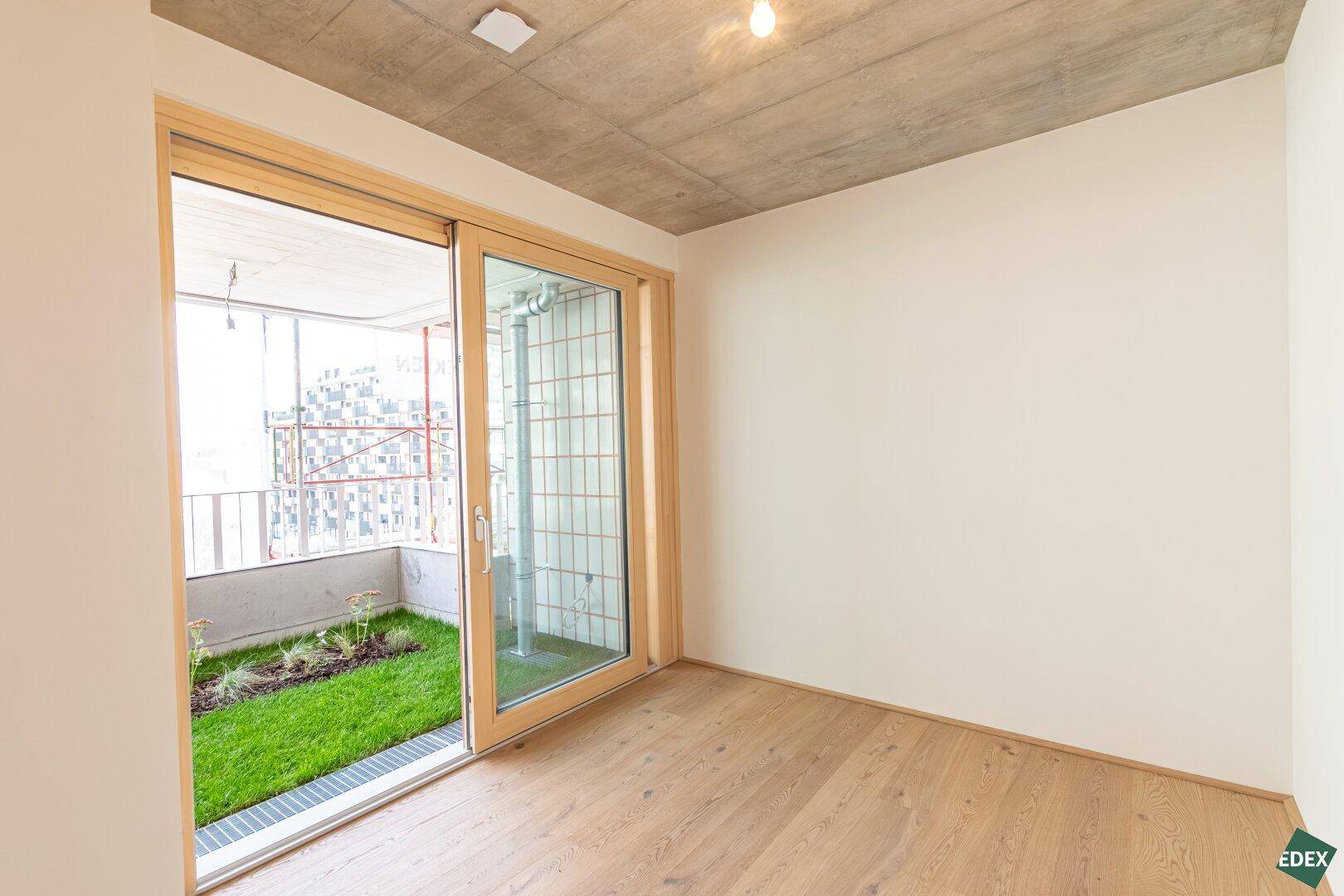 Helles Zimmer mit Schiebetür zu einem kleinen begrünten Außenbereich und Holzboden.