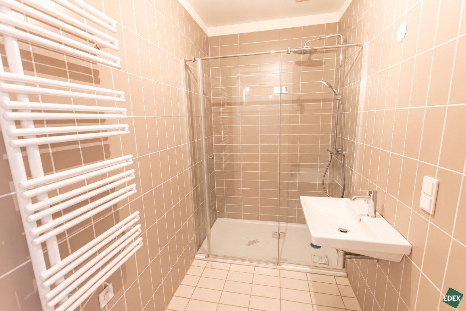 Modernes Badezimmer mit beigefarbenen Fliesen, Duschkabine und beheiztem Handtuchhalter.
