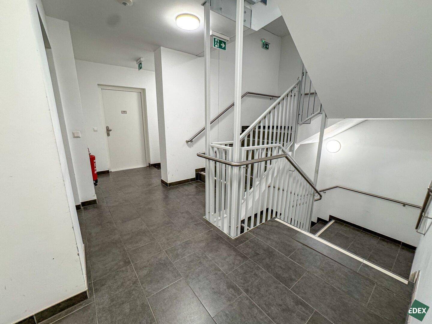 Treppenhaus mit Metallgeländer und Fliesenboden, das verschiedene Etagen des Gebäudes verbindet.