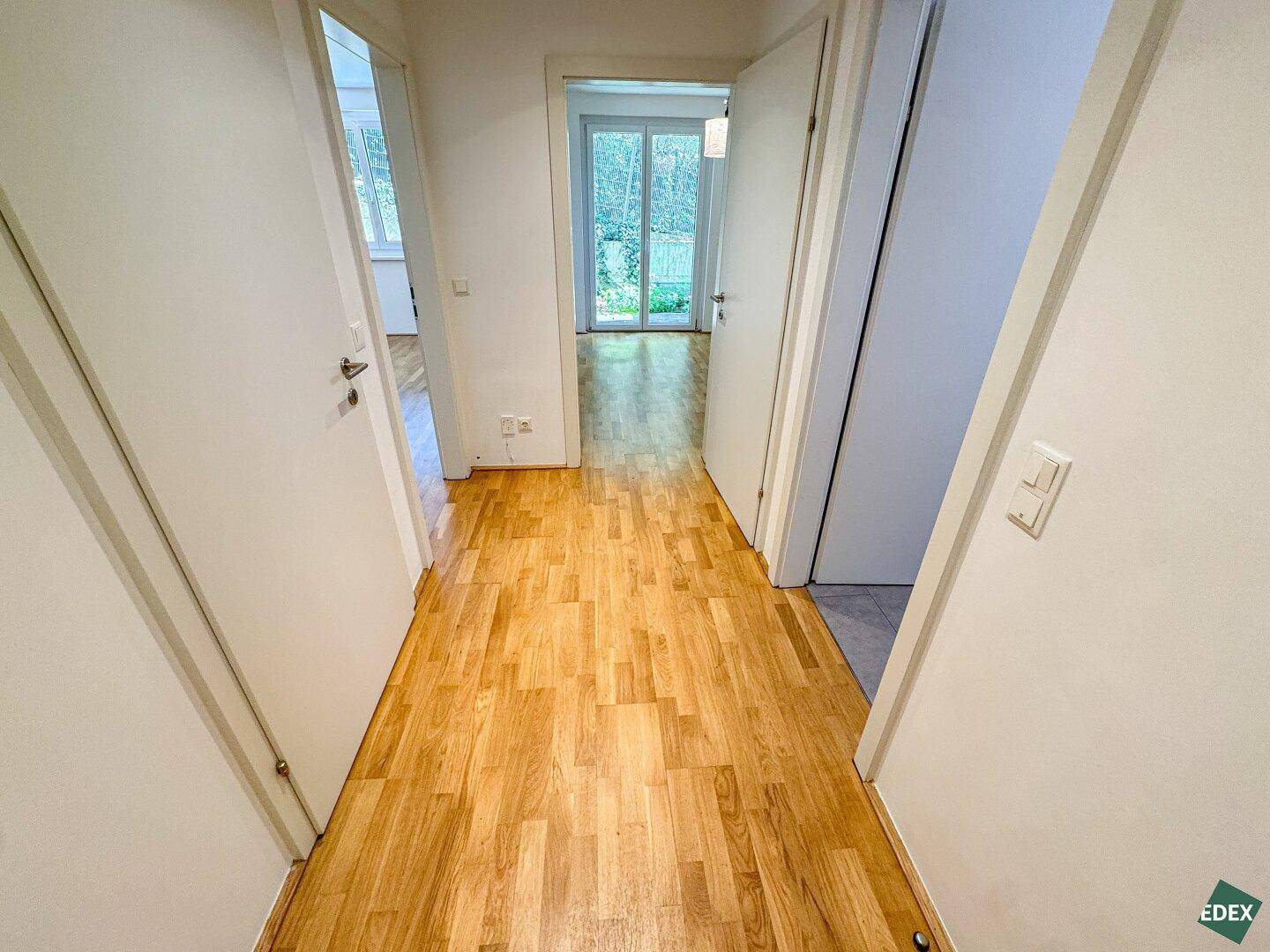Heller Flur mit Holzboden, der zu verschiedenen Zimmern und einem Außenbereich führt.