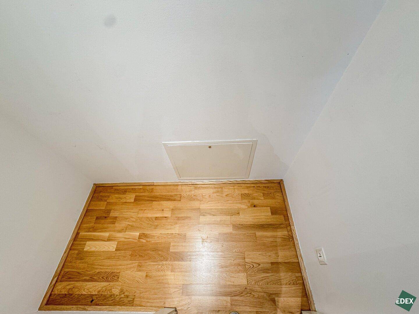 Kleiner Raum mit Holzboden und einer Zugangsluke zur Decke, möglicherweise ein Abstellraum.