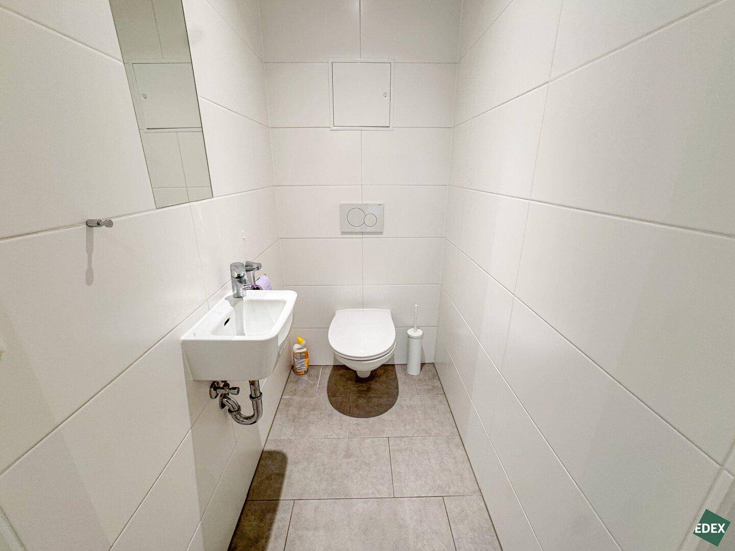 Kleines, hell gefliestes Gäste-WC mit wandhängender Toilette und kompaktem Waschbecken.