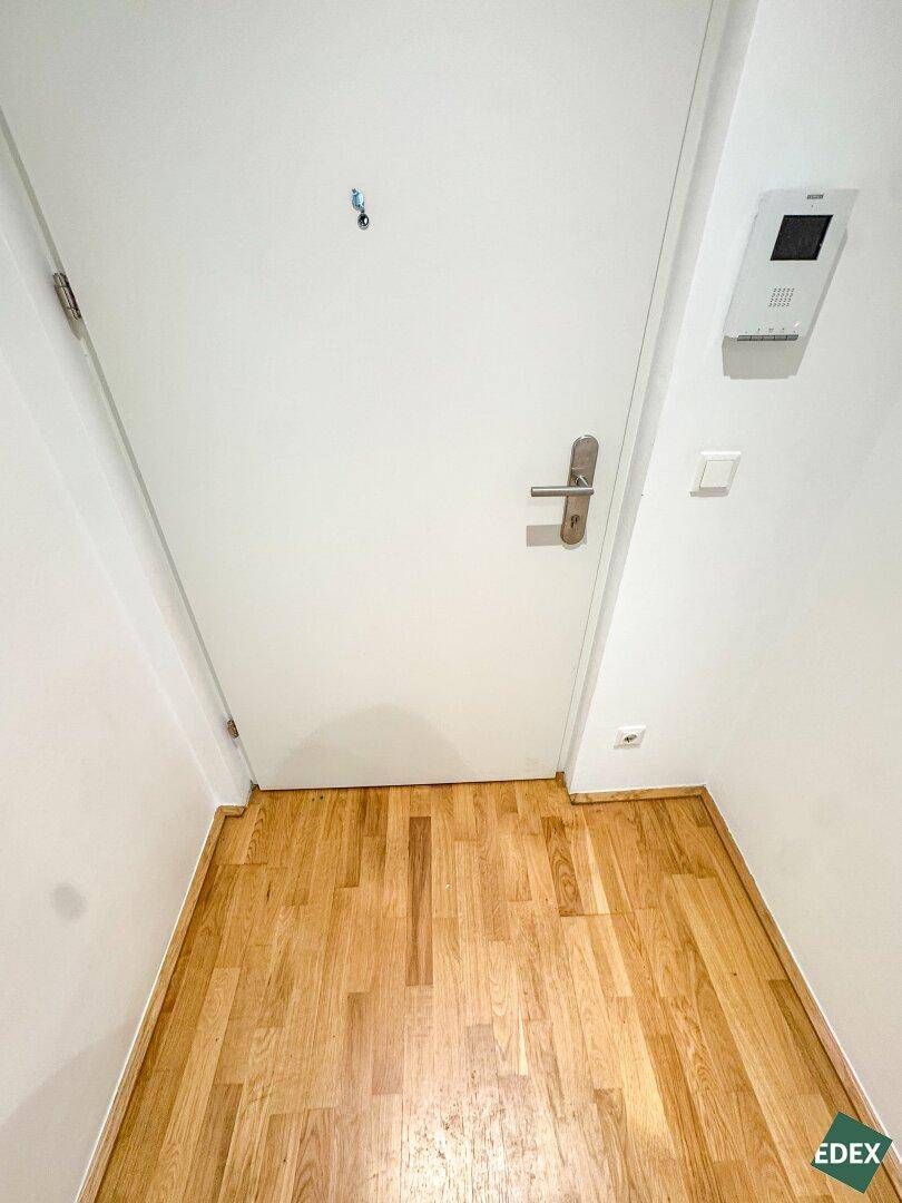 Eingangsbereich mit Holzboden, weißer Tür und Gegensprechanlage, der in die Wohnung führt.