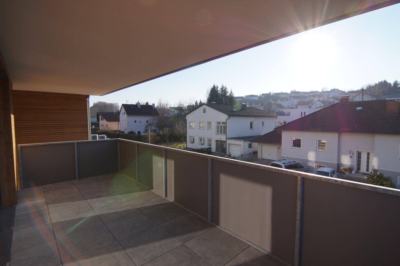 Sonniger Balkon mit Fliesenboden und Ausblick auf die umliegende Wohnsiedlung.