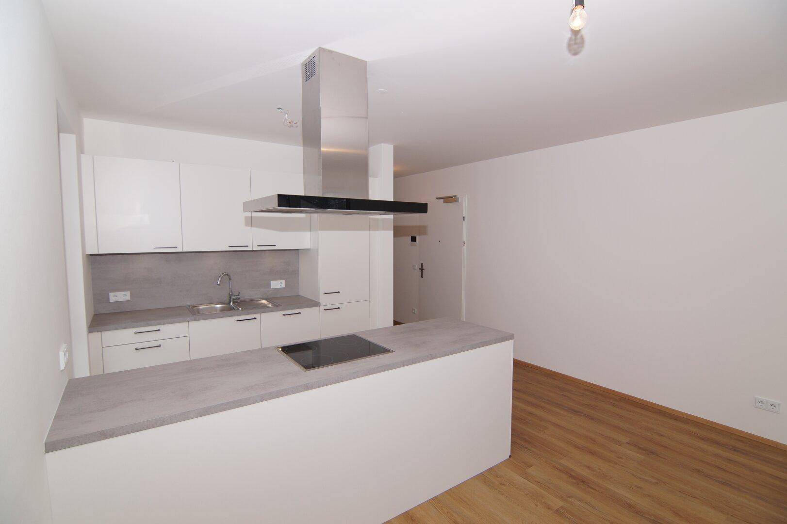 Moderne Einbauküche mit Kochinsel, Induktionskochfeld und Dunstabzugshaube in hellem Design.
