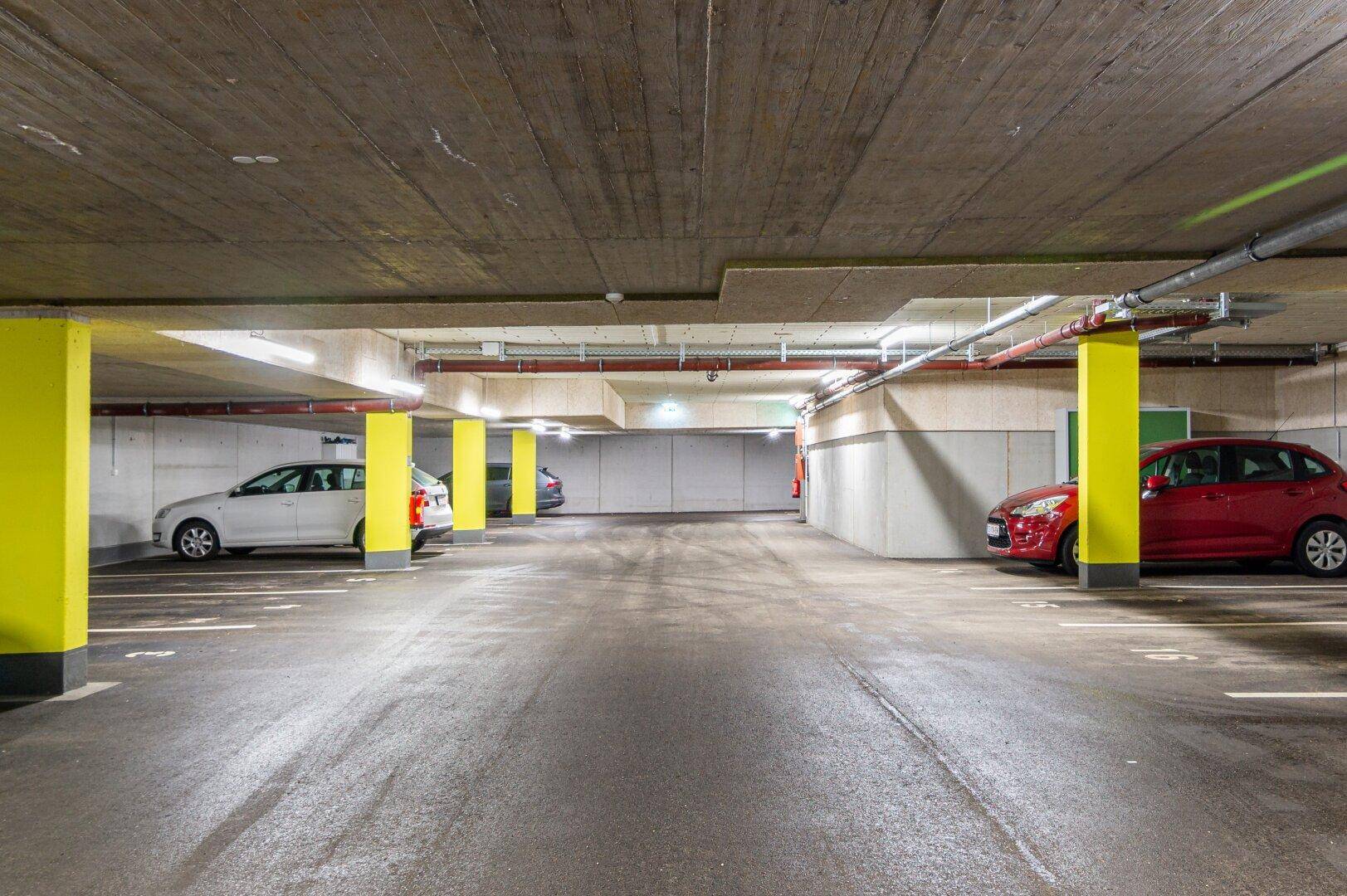 Geräumige Tiefgarage mit markierten Parkplätzen und gelben Säulen in einem Neubau.