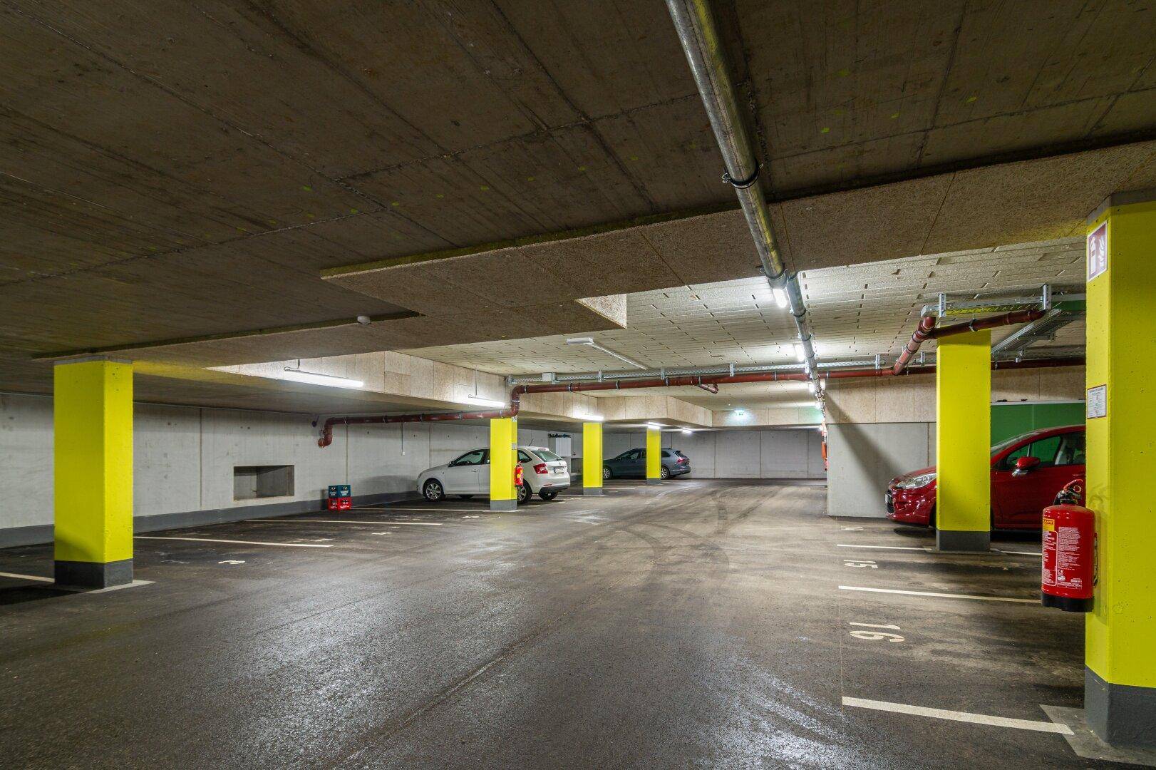 Helle Tiefgarage mit zahlreichen Parkmöglichkeiten und sichtbaren Installationen an der Decke.