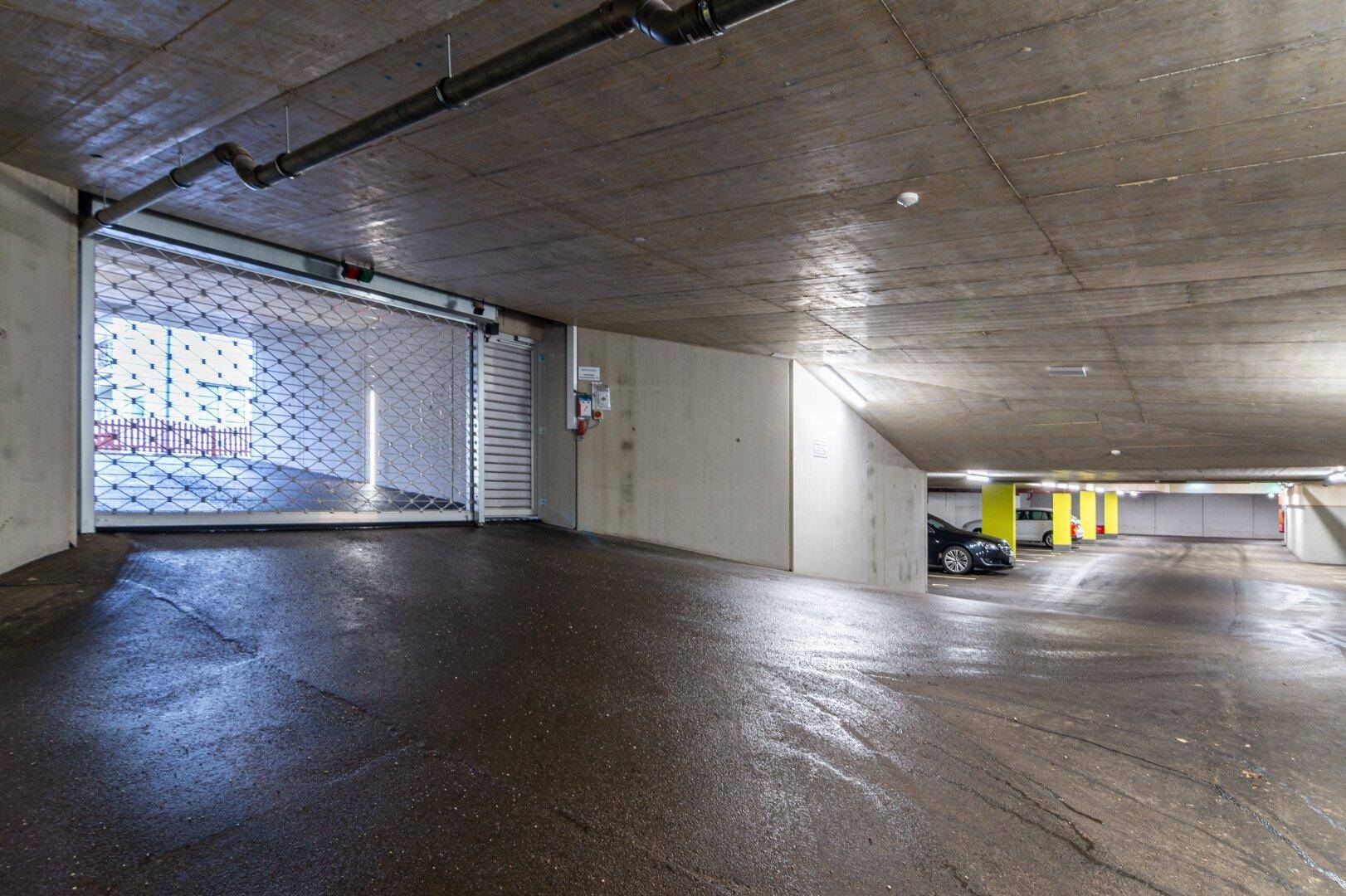 Einfahrt zur Tiefgarage mit einem geschlossenen Rolltor und weiteren Parkplätzen im Hintergrund.