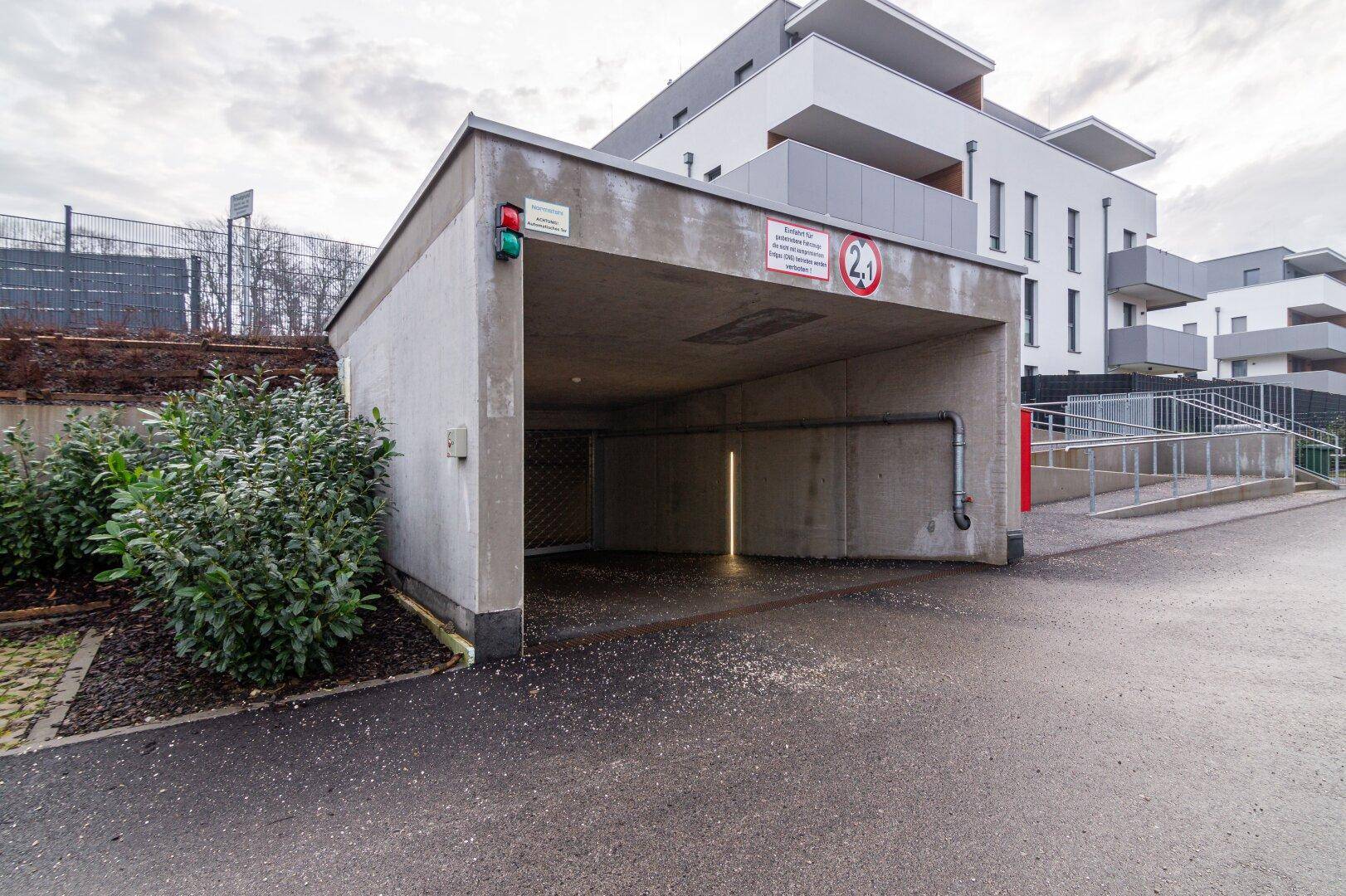 Einfahrt zur Tiefgarage mit Rampe und Ampelsystem, umgeben von modernen Wohngebäuden.