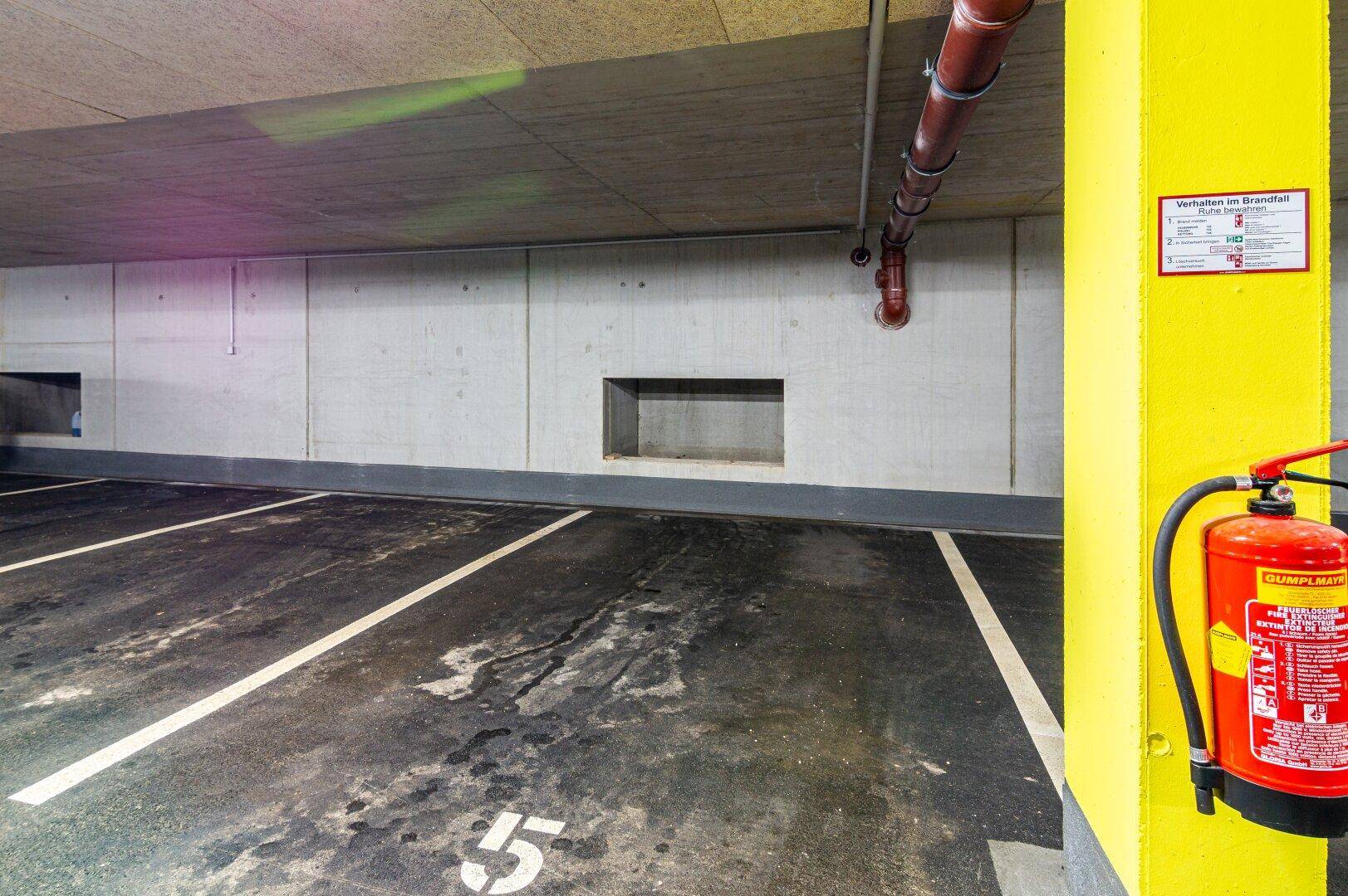 Leerer Stellplatz in der Tiefgarage mit Feuerlöscher an einer gelben Säule.