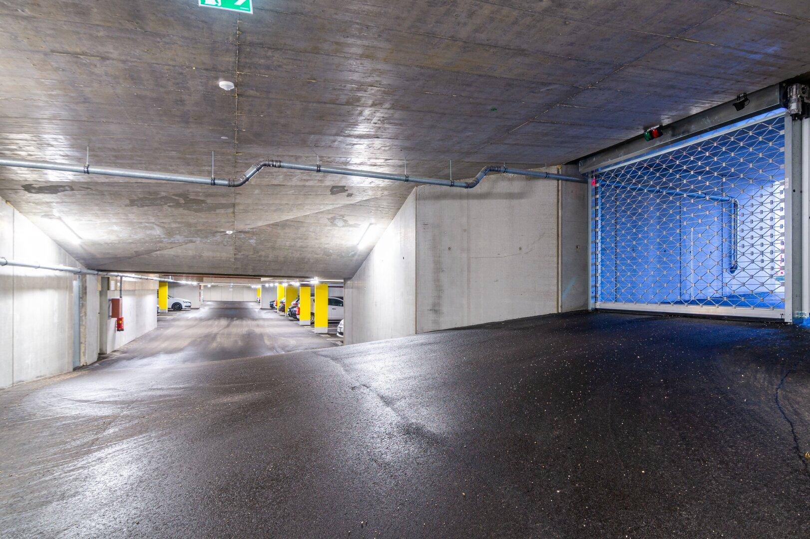 Einfahrt zur Tiefgarage mit Rolltor und Rampe, gut beleuchtet.