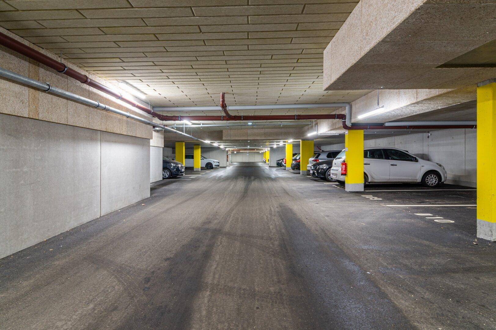Geräumige Tiefgarage mit markierten Stellplätzen, gelben Säulen und geparkten Fahrzeugen.