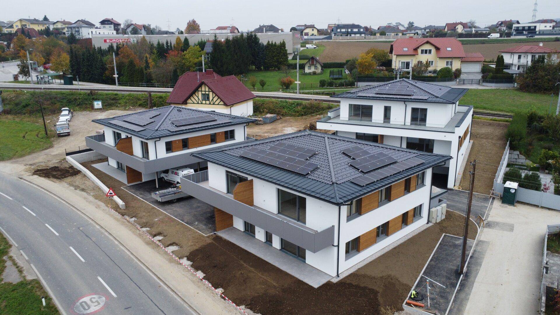 Luftaufnahme von Neubauten mit Photovoltaikanlagen auf den Dächern in ländlicher Umgebung.