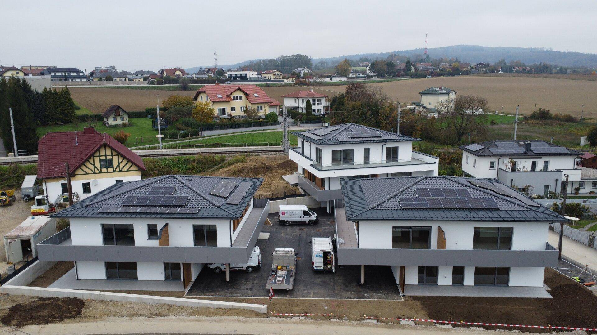Luftaufnahme von Neubauten mit Photovoltaikanlagen auf den Dächern in ländlicher Umgebung.