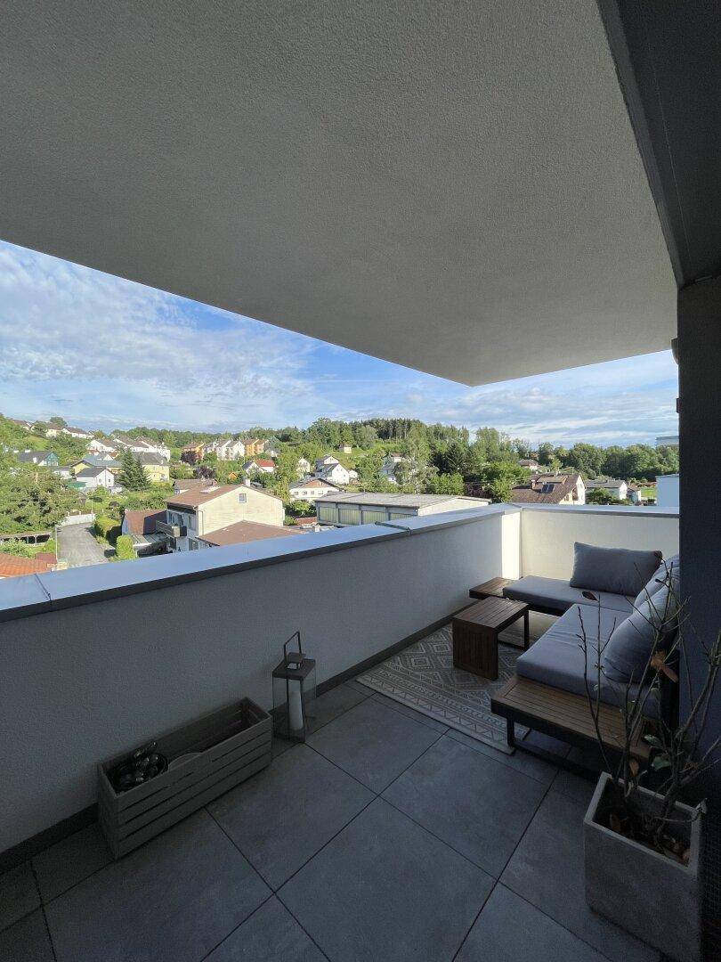 Sonniger Balkon mit Lounge-Möbeln und Blick auf die grüne Wohngegend im Sommer.