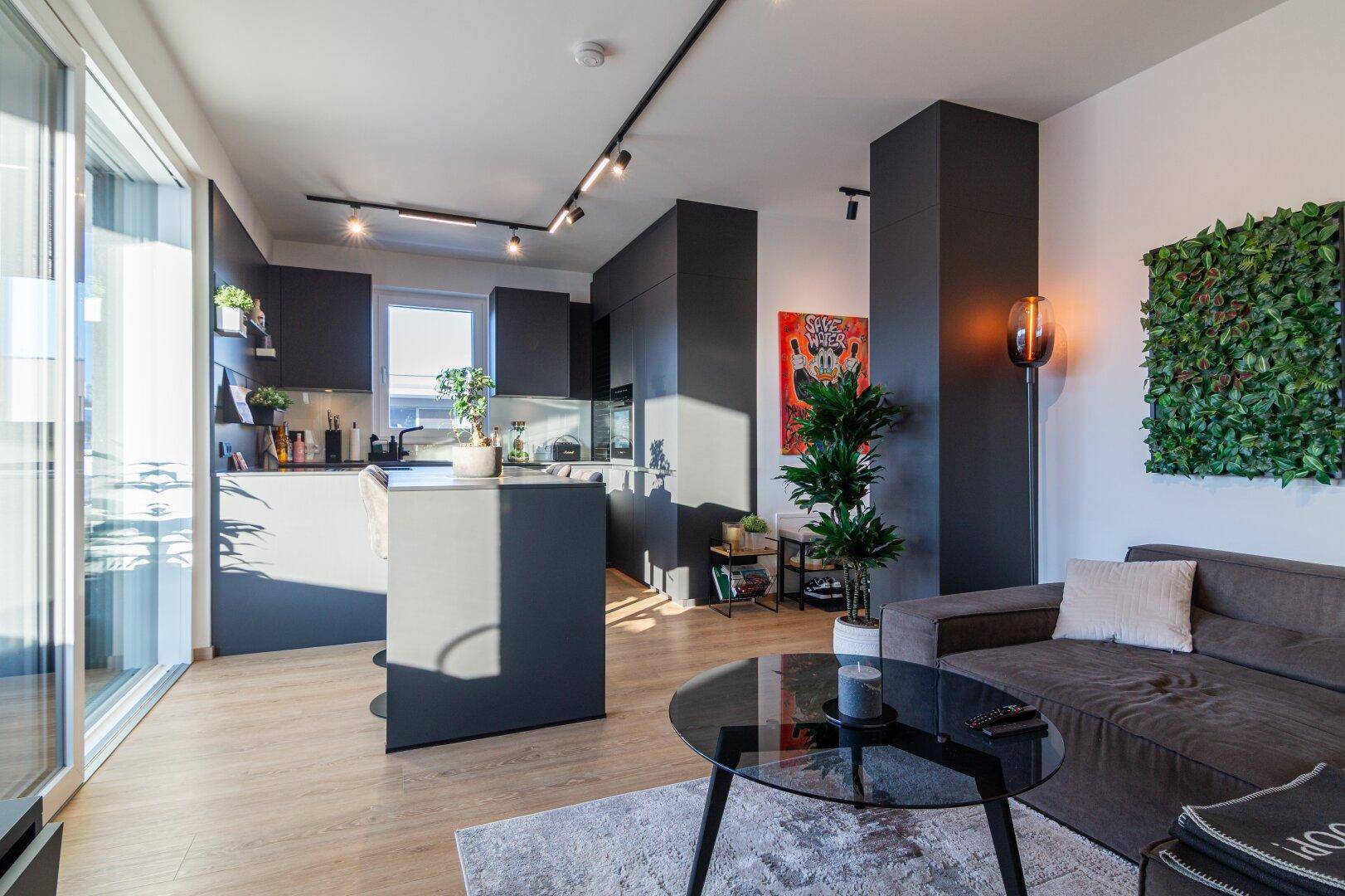 Offener Wohn- und Essbereich mit moderner Küche, Holzboden und Zugang zum Balkon.