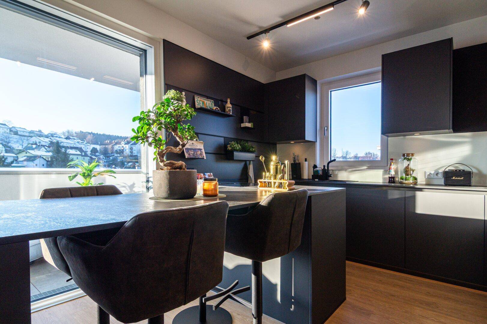 Moderne Küche mit dunklen Schränken, Kücheninsel und Blick auf die verschneite Landschaft.