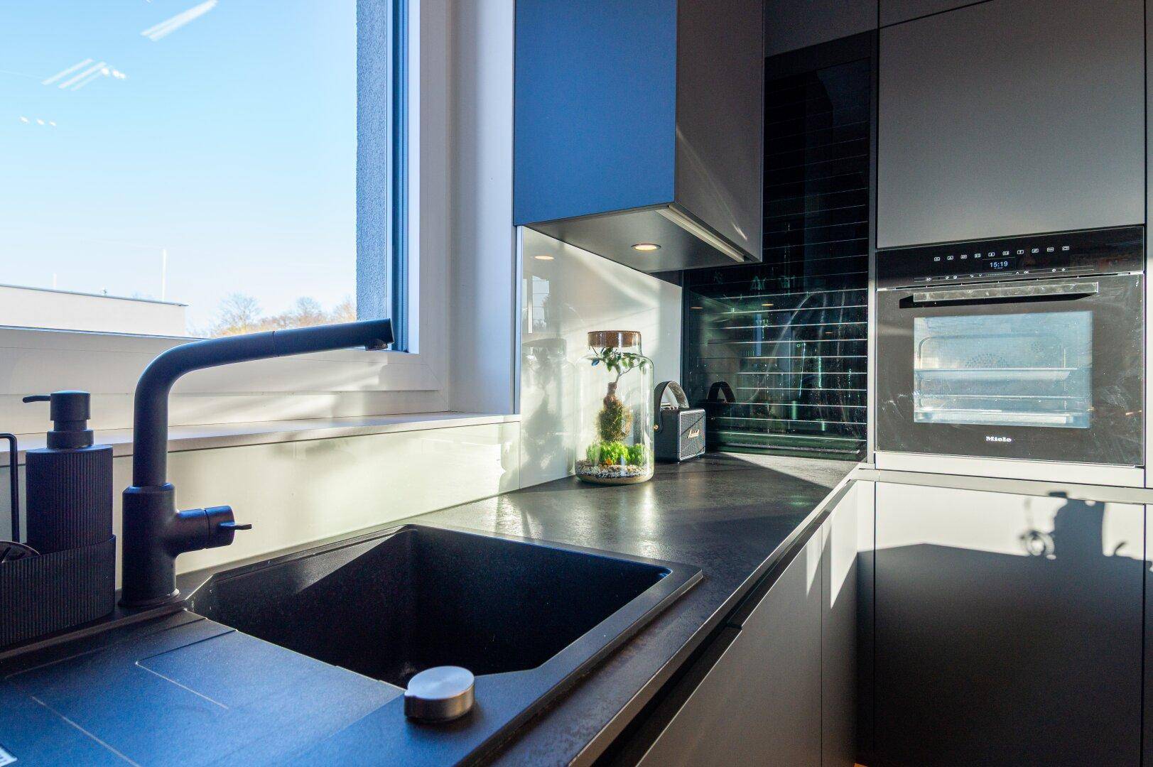 Moderner Spülbereich in der Küche mit schwarzem Waschbecken und Armatur unter dem Fenster.