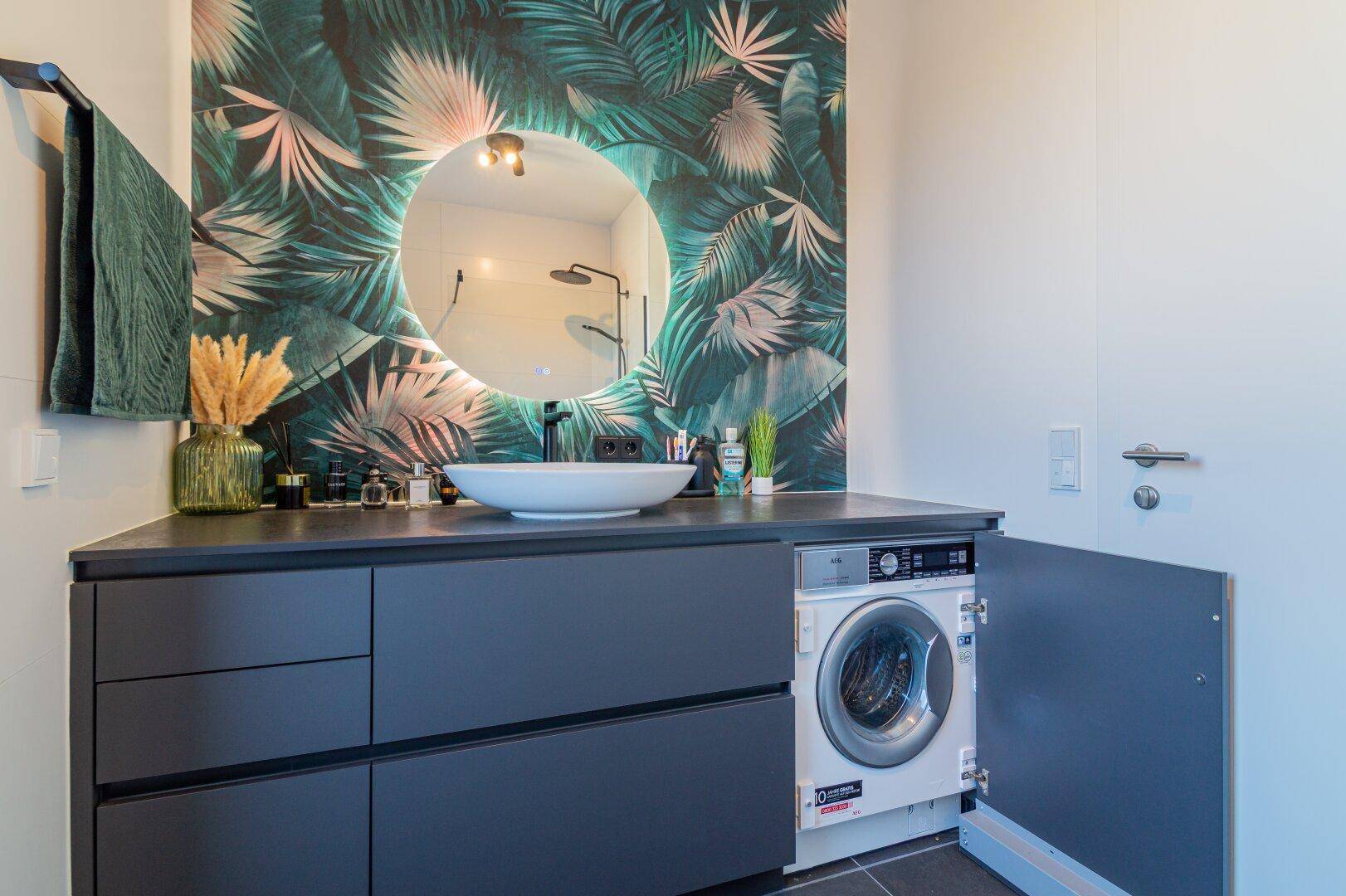 Modernes Badezimmer mit Waschtisch, beleuchtetem Spiegel und integrierter Waschmaschine.