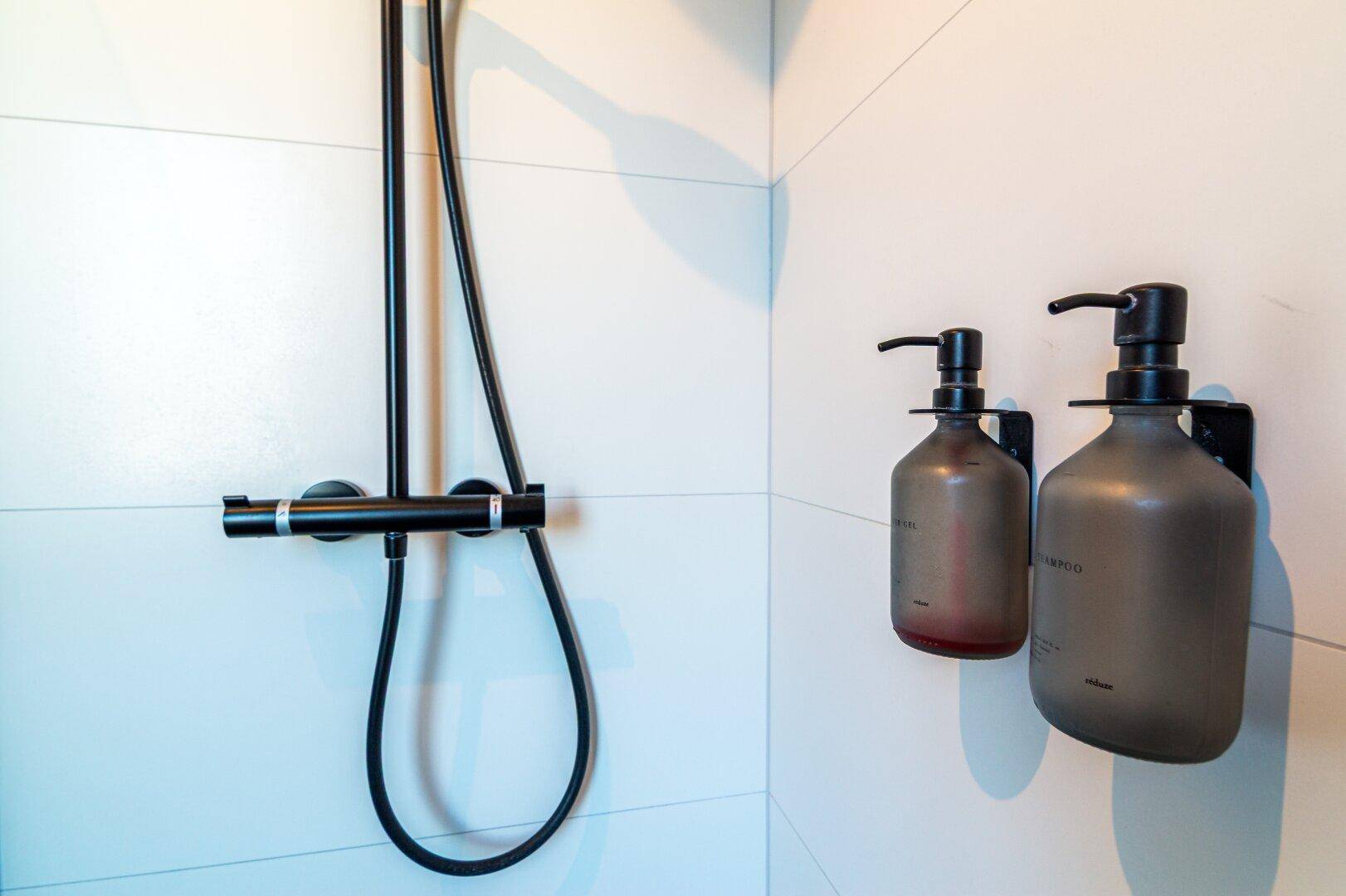 Detailansicht der modernen Regendusche mit schwarzer Armatur und weißen Fliesen.