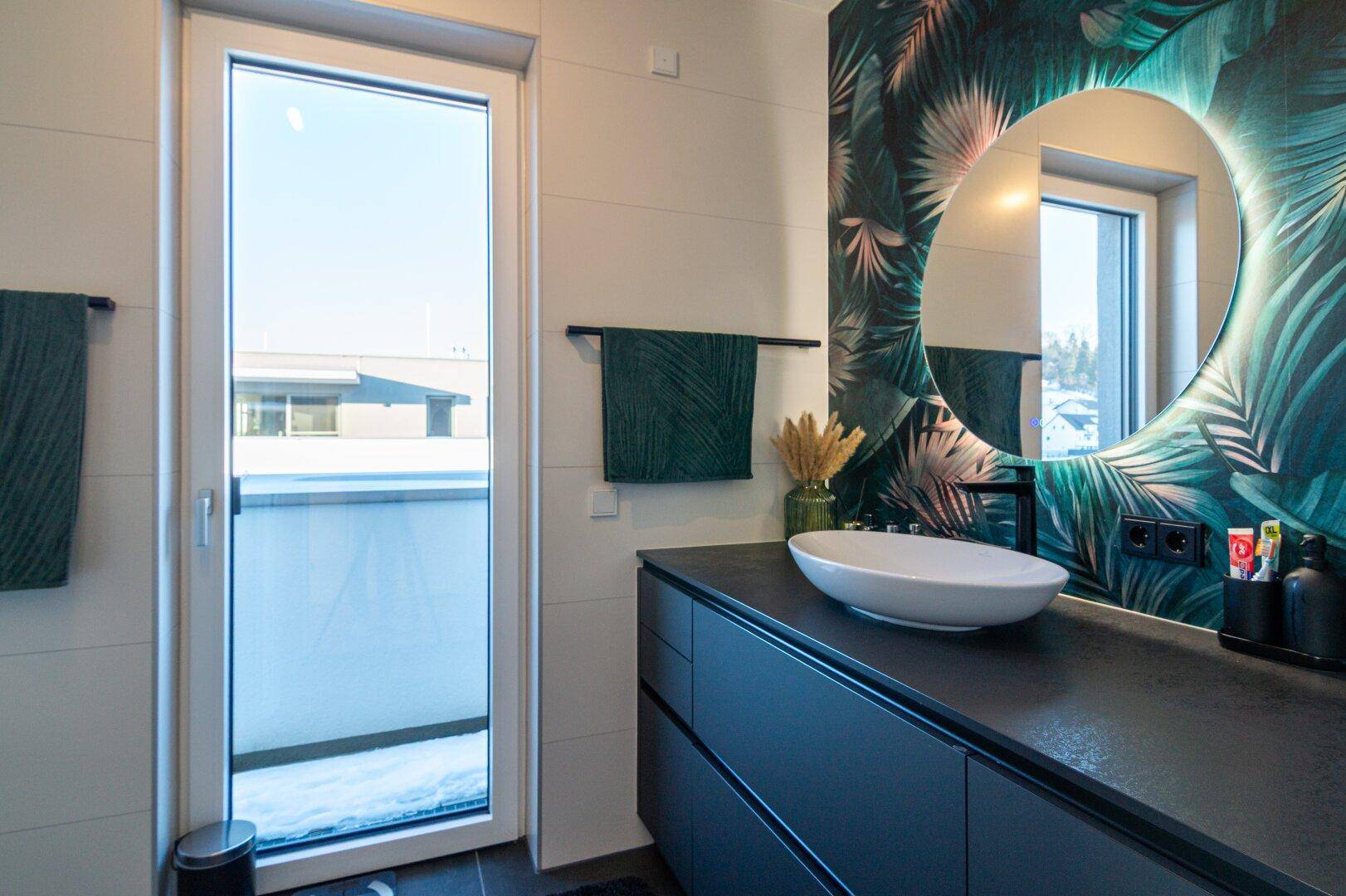 Modernes Badezimmer mit Waschtisch, beleuchtetem Spiegel und Zugang zum Balkon.