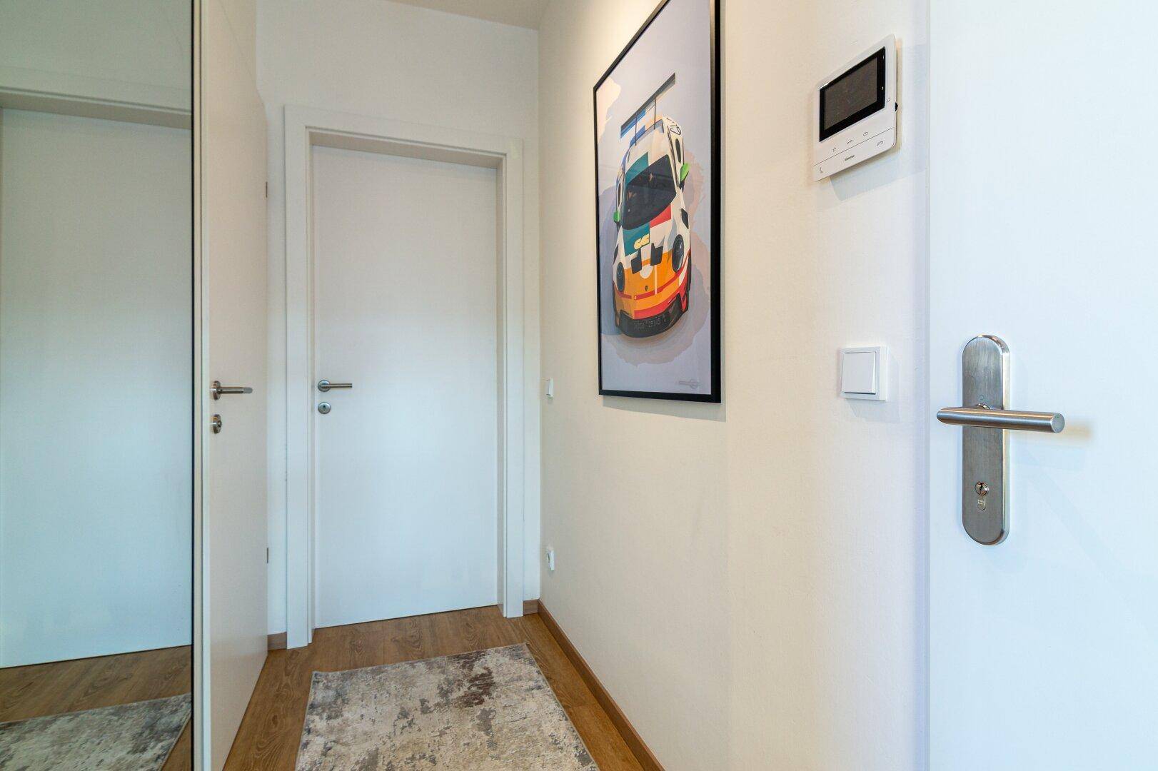 Heller Flur mit Holzboden, weißer Tür und einem modernen Kunstwerk an der Wand.