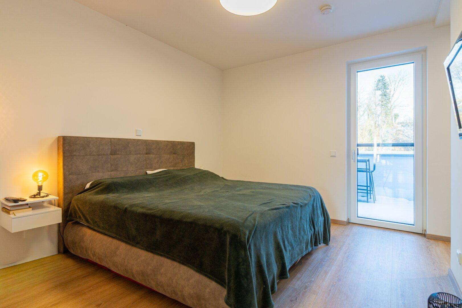 Helles Schlafzimmer mit Doppelbett, Holzboden und Zugang zu einem Balkon.