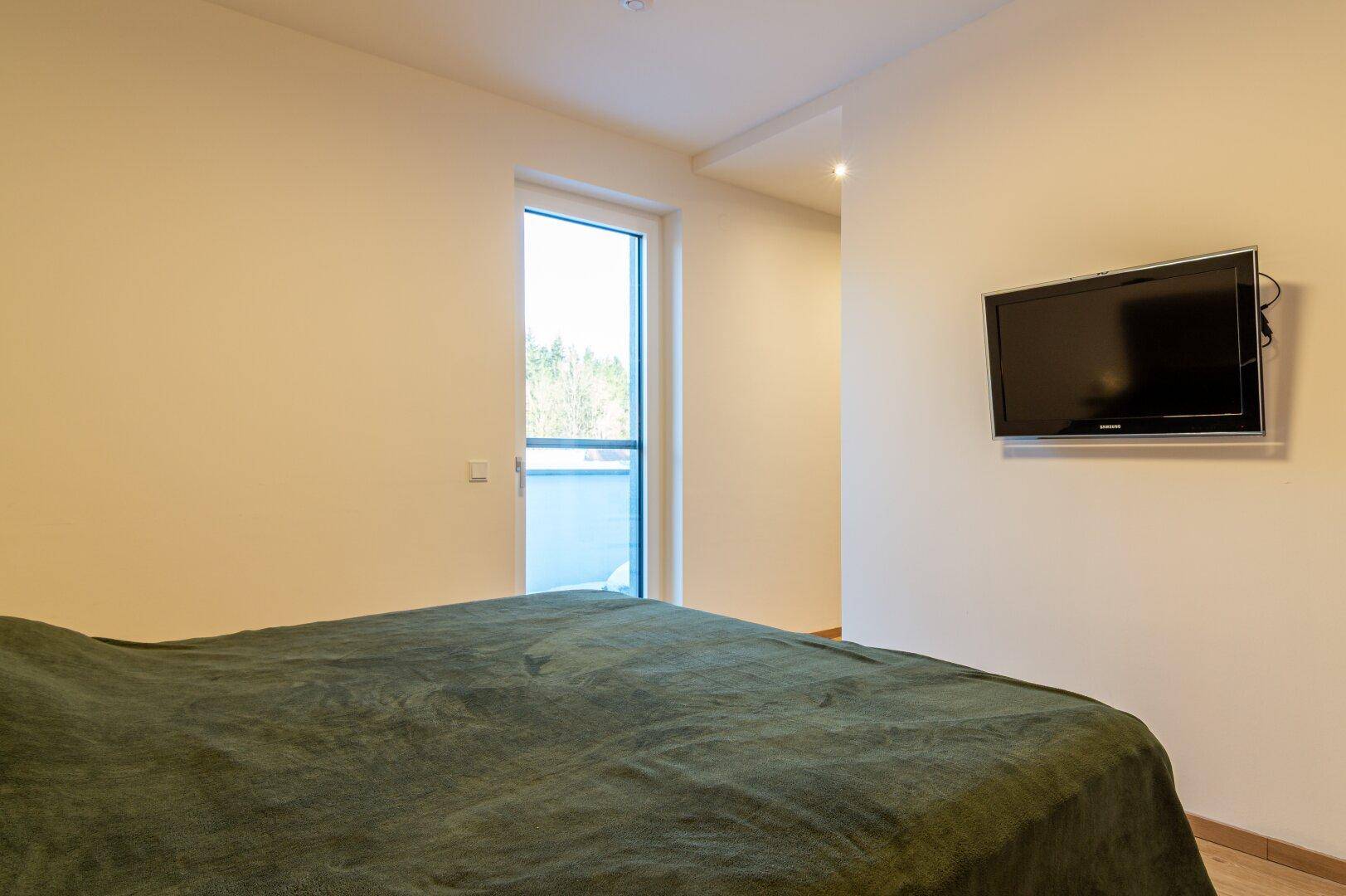 Helles Schlafzimmer mit Doppelbett, Holzboden und Zugang zu einem Balkon.