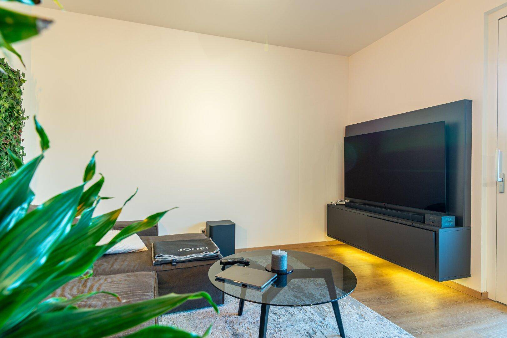 Gemütlicher Wohnbereich mit Sofa, Couchtisch und großem Fernseher an der Wand.