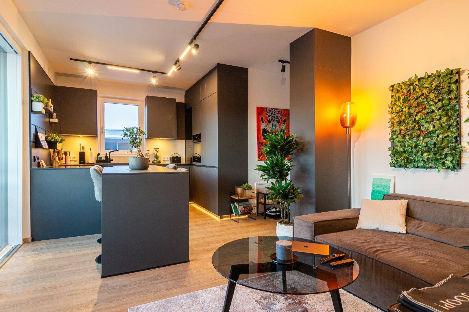 Offener Wohn- und Essbereich mit moderner Küche, Holzboden und Zugang zum Balkon.