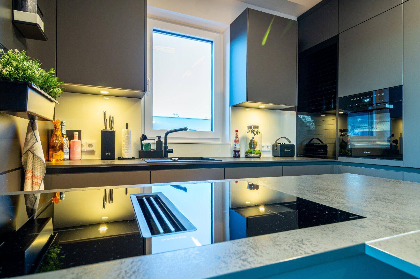 Detailansicht der modernen Küche mit Induktionskochfeld, Backofen und Fenster.