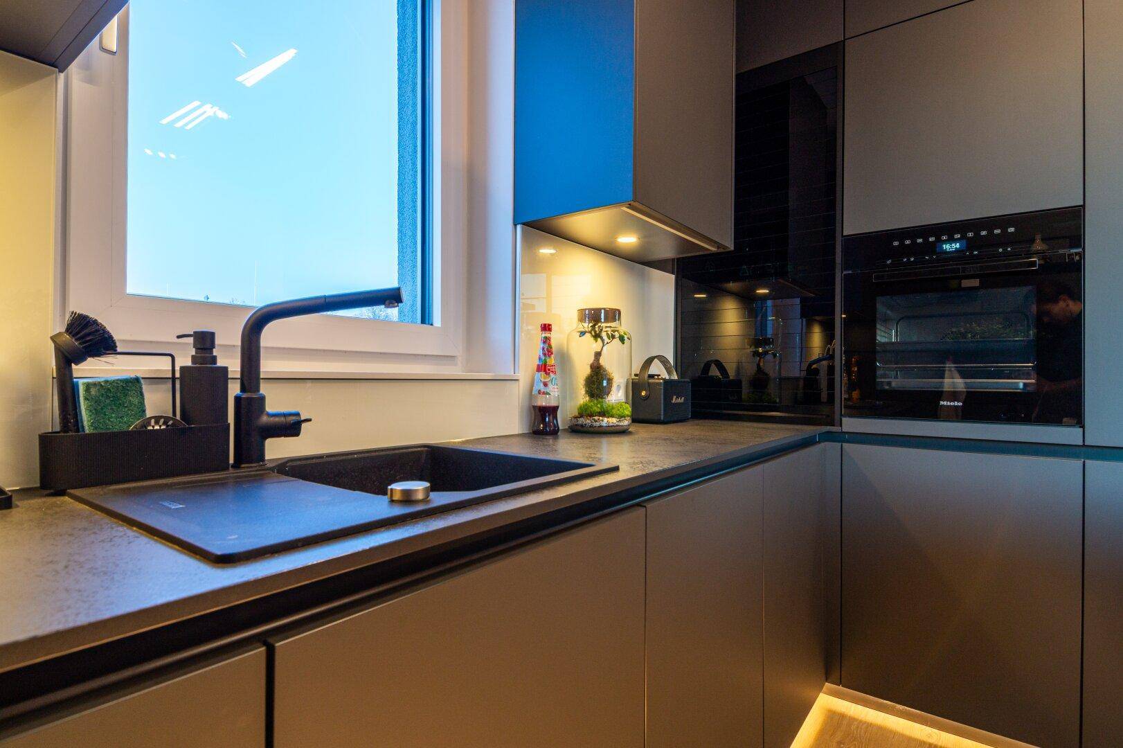 Moderner Spülbereich in der Küche mit schwarzem Waschbecken und Armatur unter dem Fenster.