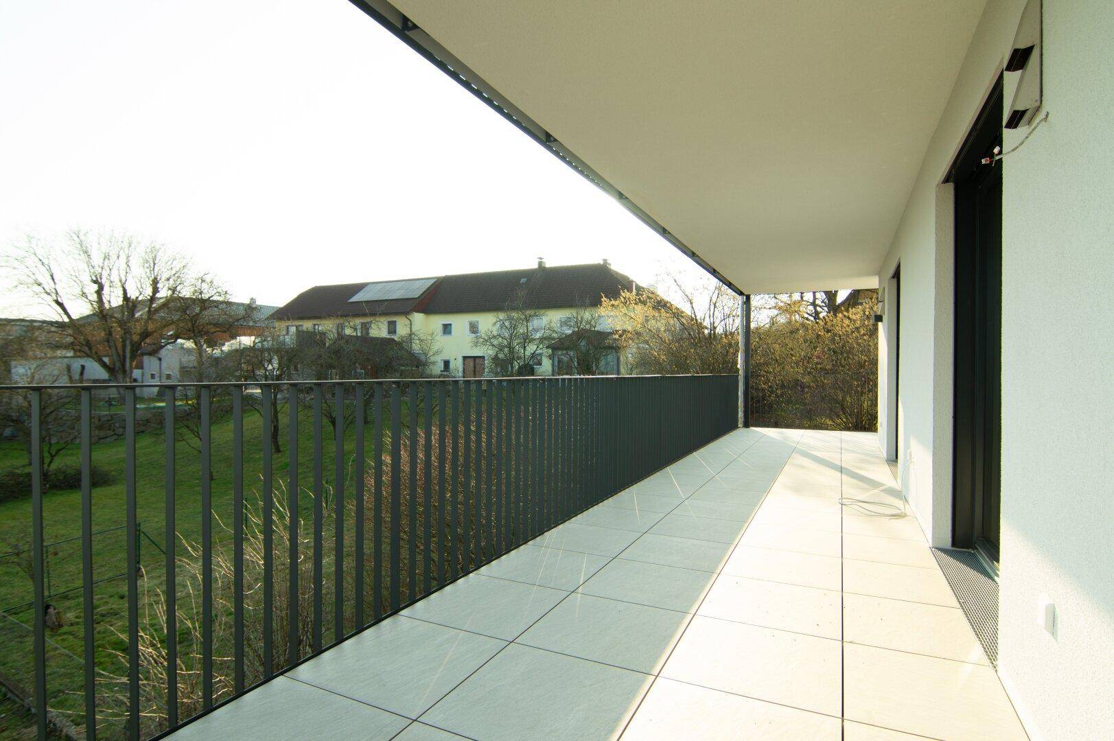 Langer Balkon mit hellen Fliesen und Blick auf ein traditionelles Gebäude in der Ferne.