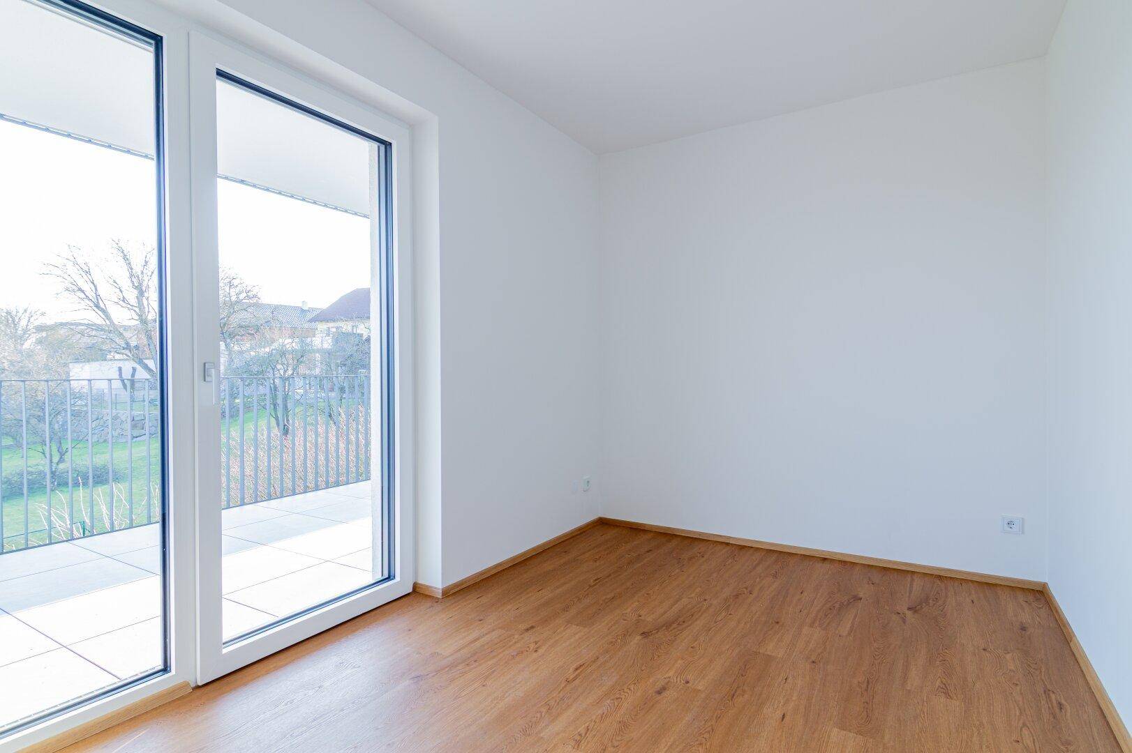 Freundliches Zimmer mit Holzboden und direktem Zugang zum Balkon, bietet viel Helligkeit.