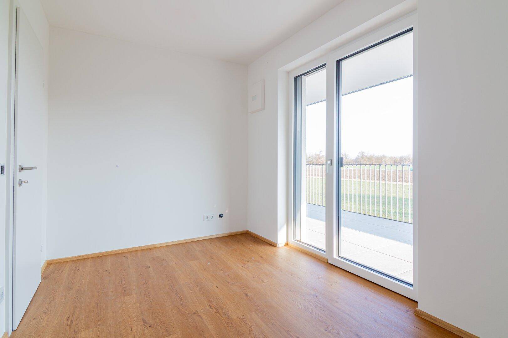 Modernes Zimmer mit Holzboden und Balkonzugang, ideal für viel Tageslicht und frische Luft.