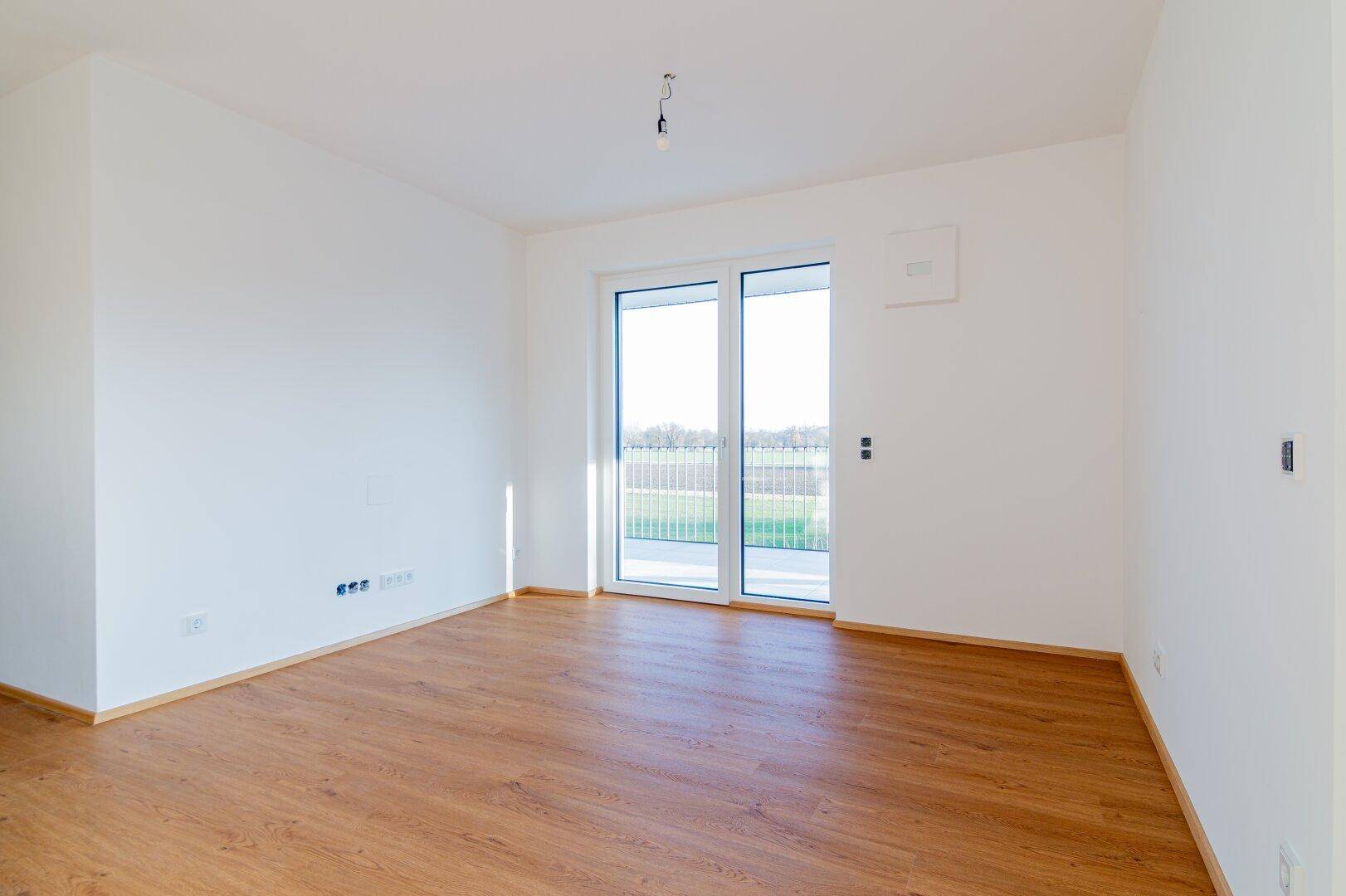 Geräumiger, heller Raum mit Holzboden und Schiebetür zum Balkon, ideal für viel Tageslicht.