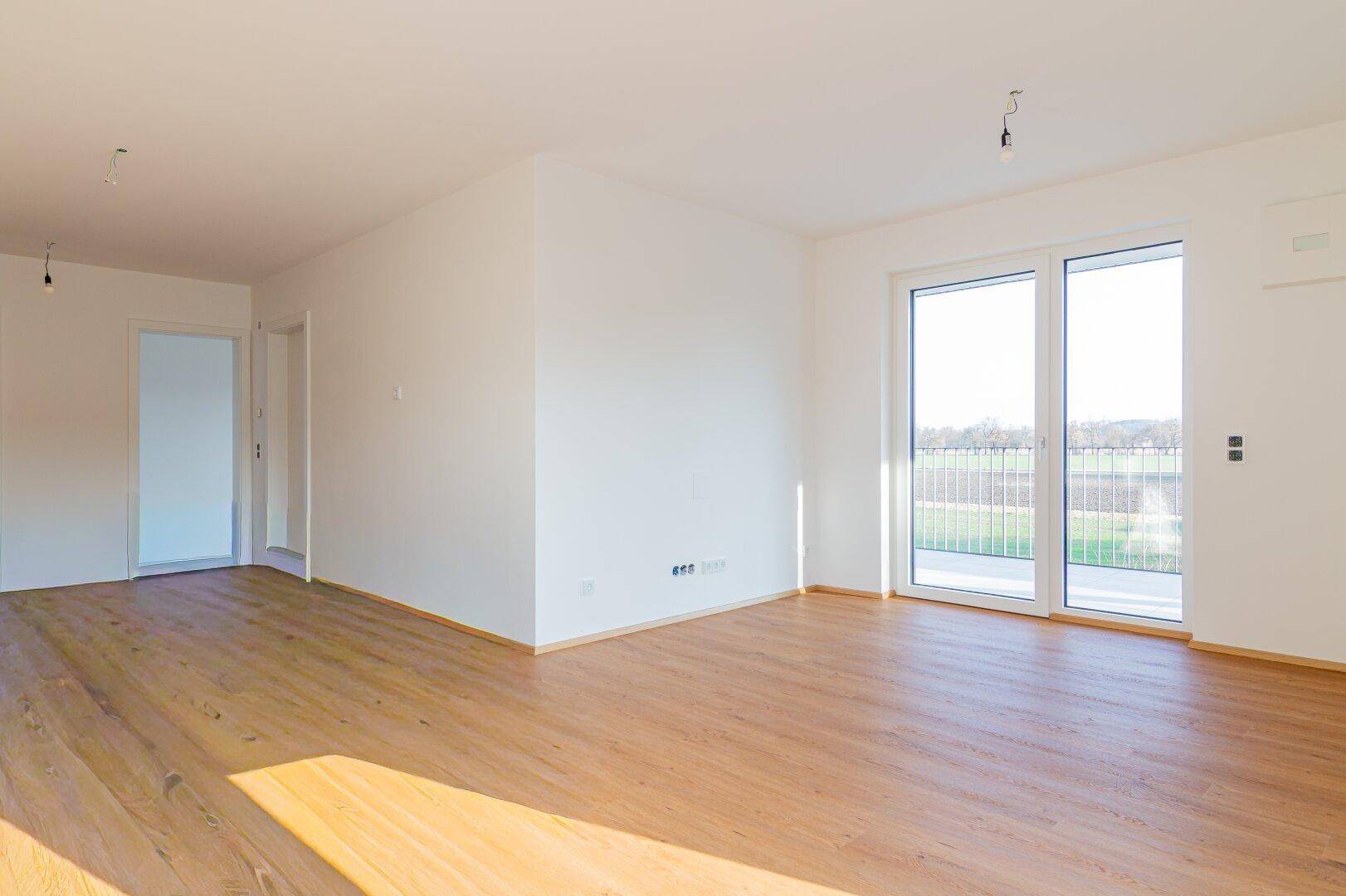 Heller Raum mit Holzboden und Zugang zu einem Balkon, der einen weiten Ausblick bietet.